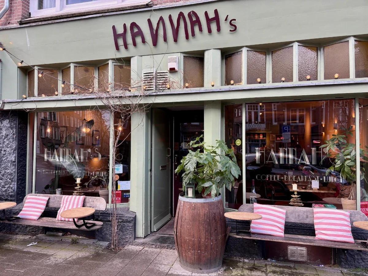 Cafe with HANNAH's sign above the entrance and large windows with bench seating and red and white striped pillows