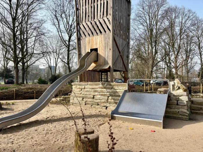 Large wooden enclosed tower with long metal wavy slide and lower, wider slide beside
