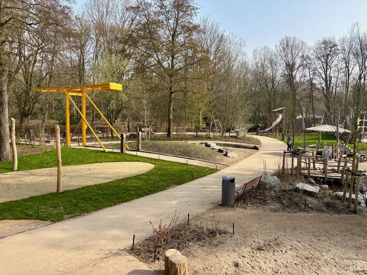 Nature playground with yellow bridge and various play structures along a dirt path