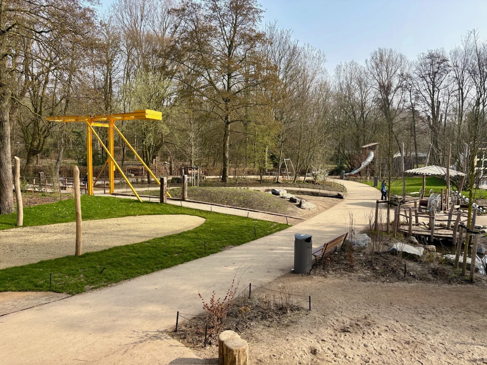 Nature playground with yellow bridge and various play structures along a dirt path
