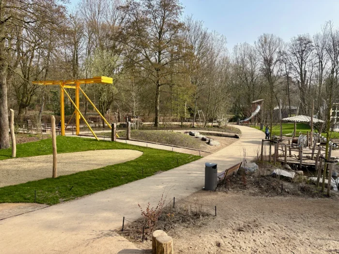 Nature playground with yellow bridge and various play structures along a dirt path