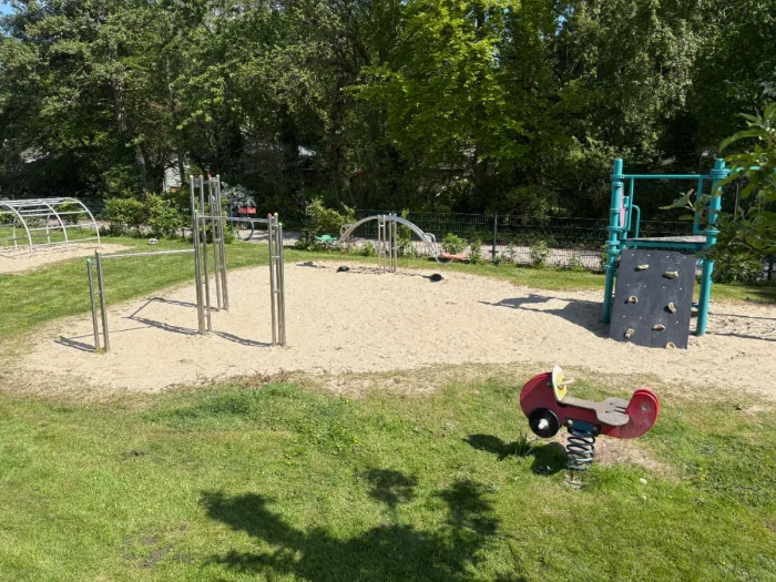 Sunny playground with varied play equipment including small climbing structure and red vehicle rocker