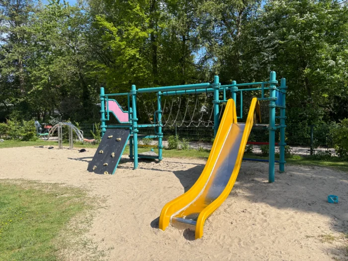 Green metal climbing structure with yellow slide set in forested area