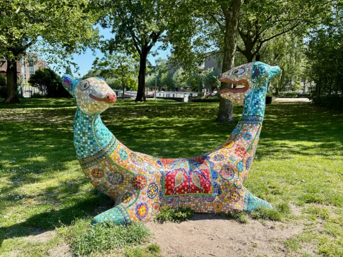 Two-headed animal sculpture covered in colorful mosaic tiles in park setting