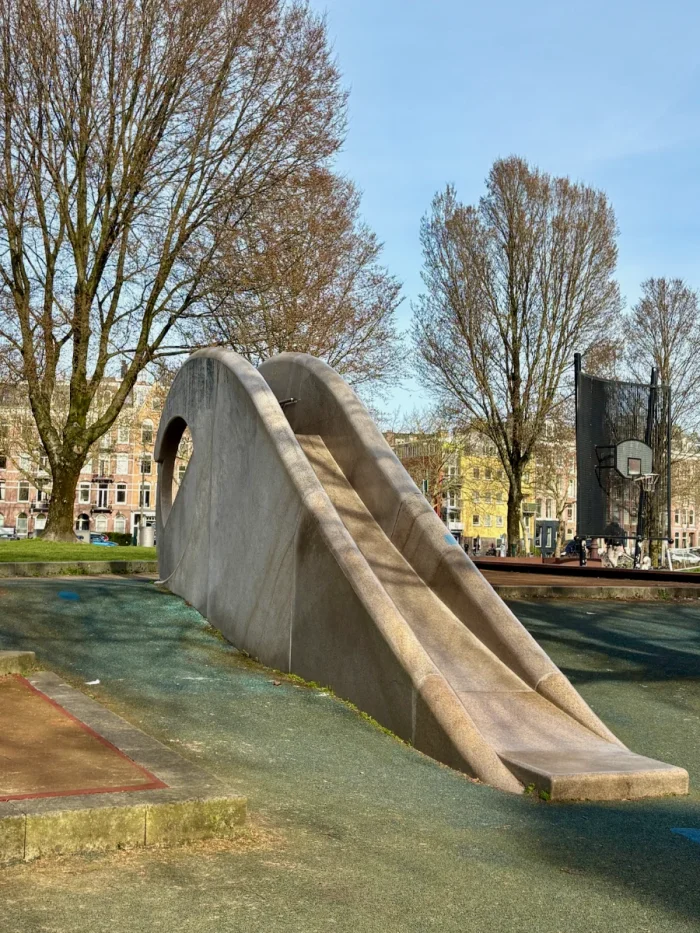 Contemporary sculptural concrete slide with rounded edges and large mature winter trees around