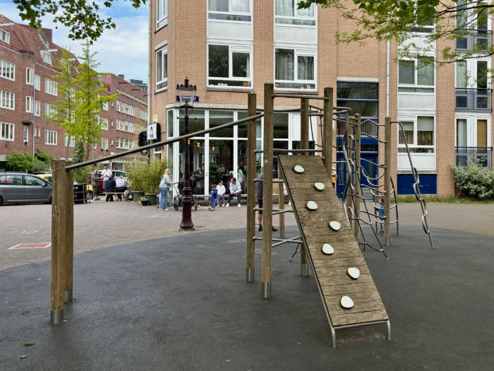 Wood and metal climbing structure on plaza with coffee shop behind