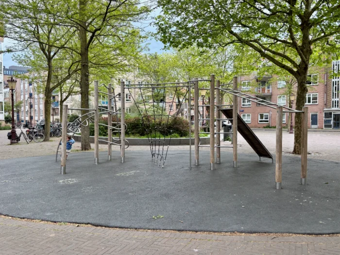 Large climbing structure with a variety of ladders, ropes, and monkey bars set in shady plaza in residential area