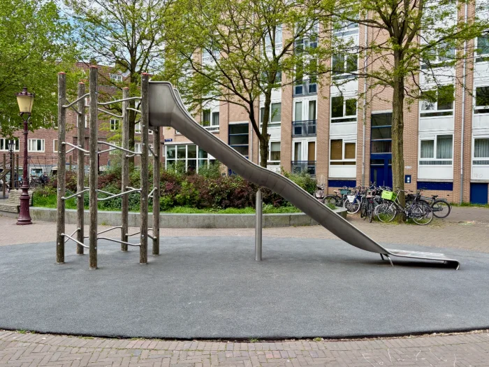 Tall climbing structure with long metal slide set in residential plaza