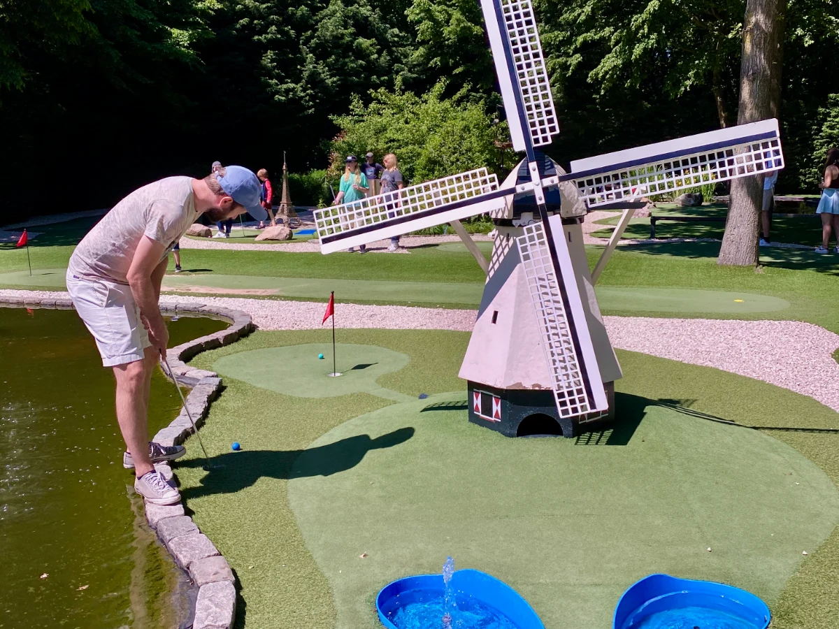 Man putting on mini golf course with windmill and water feature