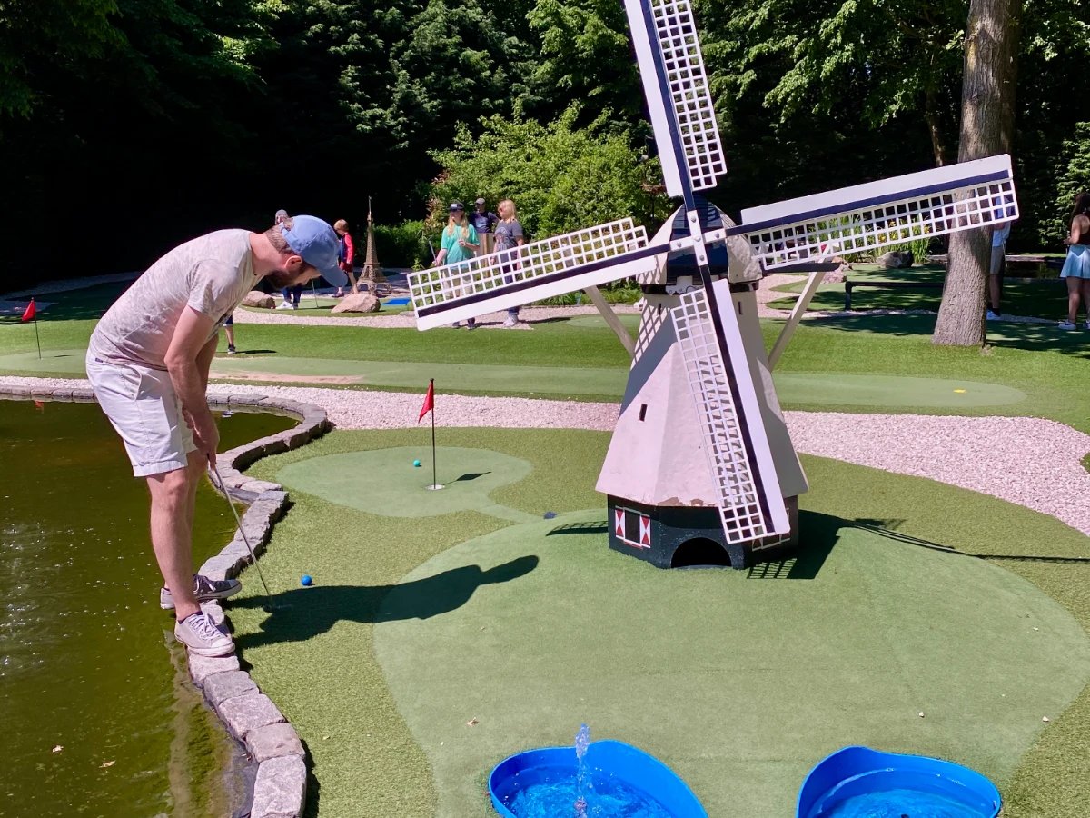 Man putting on mini golf course with windmill and water feature
