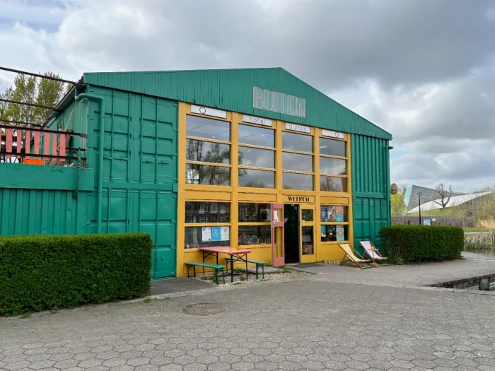 Green-painted warehouse with large, yellow-painted windows and BUITEN written in neon above the entrance