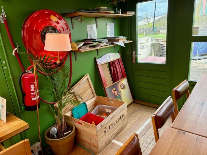 Play corner with a chest of toys, and shelf with books in a green-walled corner of a restaurant