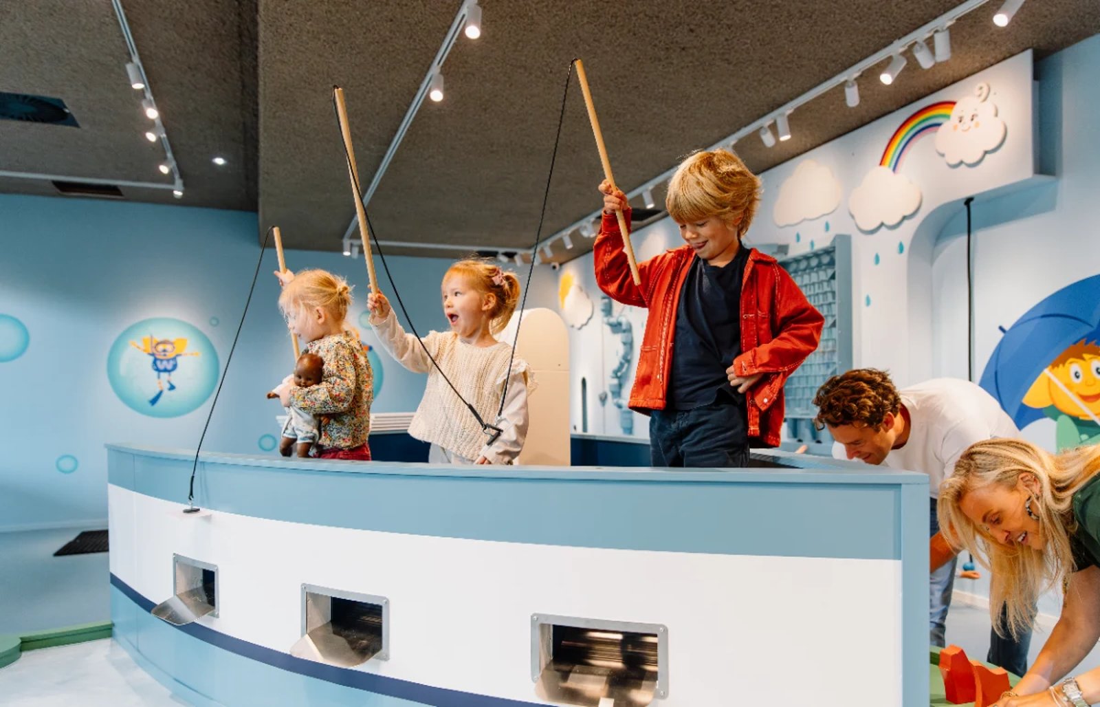 Young kids holding toy fishing poles with magnets on the end while standing in a blue pretend boat