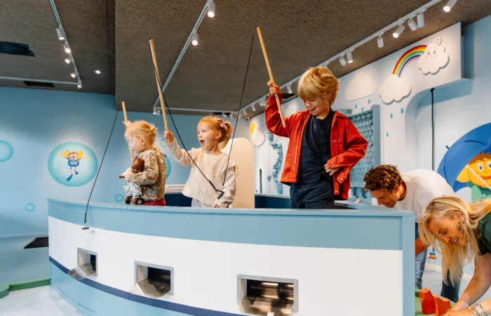 Young kids holding toy fishing poles with magnets on the end while standing in a blue pretend boat