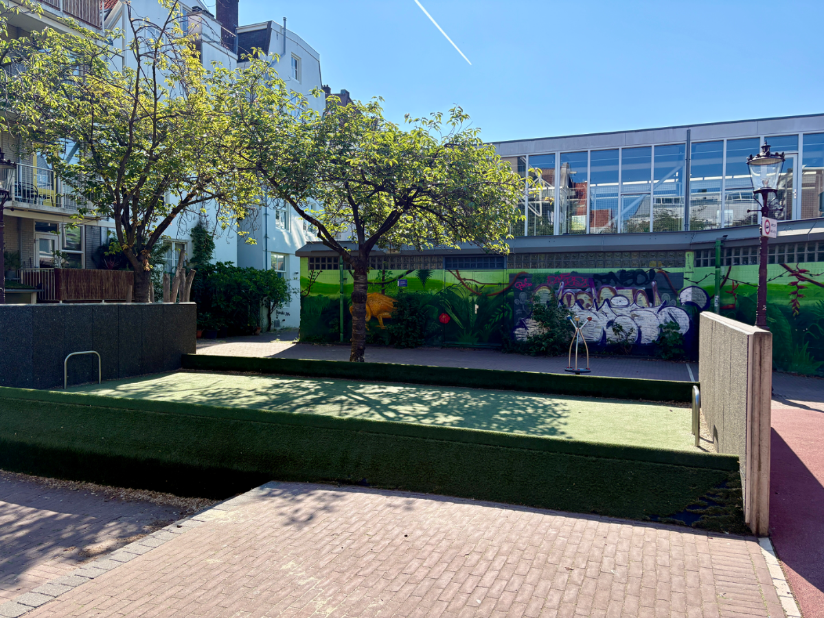 Mini football pitch with trees and brick building with mural behind