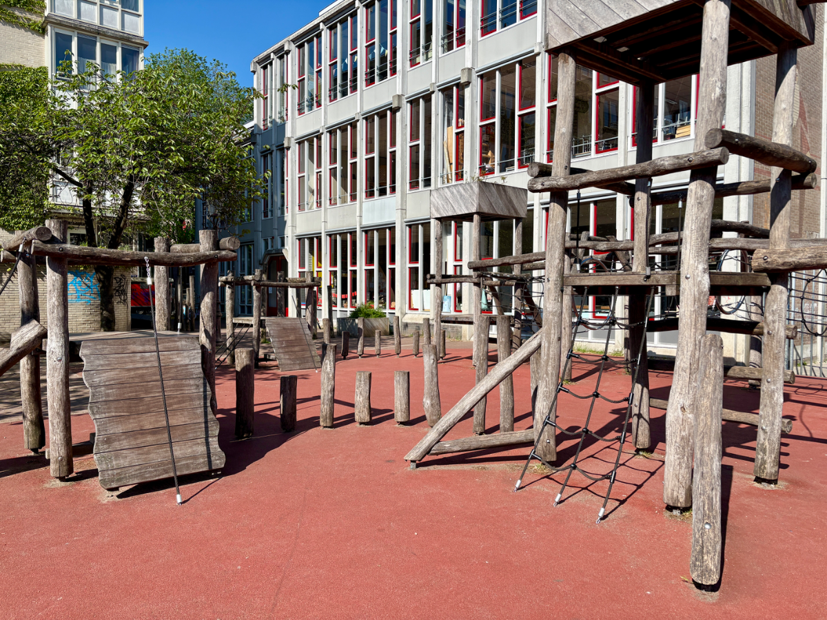 Wooden climbing structure with ramp and rope climbing net and large residential building behind