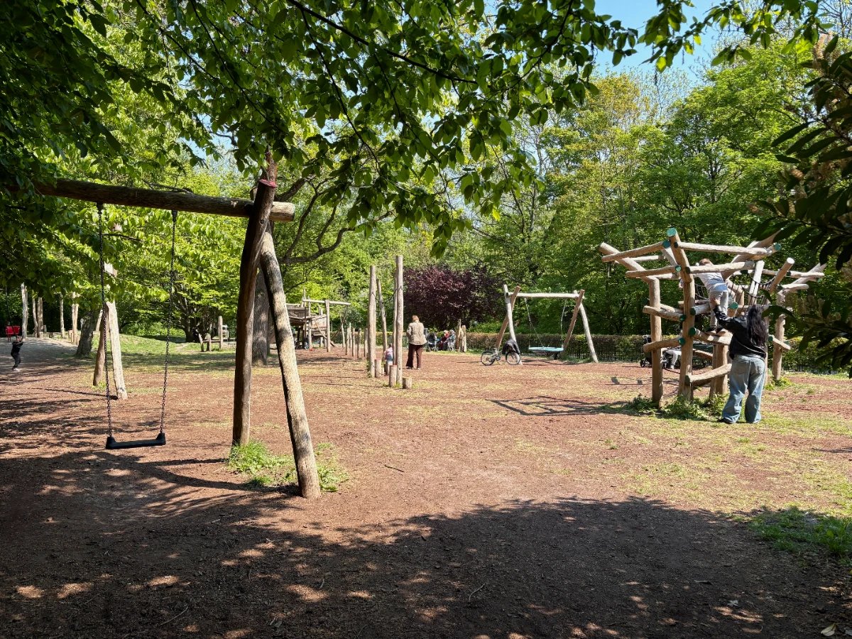 Kids and parents play on shaded playground with swing and natural climbing structures