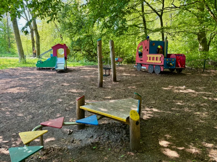 Shaded playground for small children with colorful slide, baby swing, triangle balance beam, and play fire truck