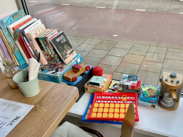 Collection of books, games, and toys arranged on a window ledge next to a wooden table with menu