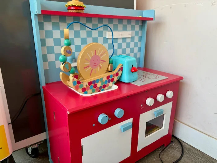 Bright red, blue, and white play kitchen with mini blue toaster and children's bead toy on the counter