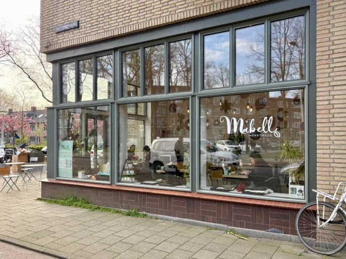 Storefront with large steel windows and light brick building with "Mabell" written on the glass