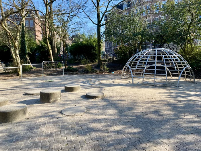 Shaded plaza with metal jungle gym and concrete stepping stones with trees behind