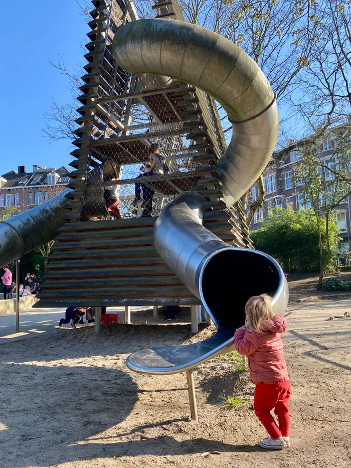 Girl at the bottom of a big spiral slide with wooden and metal mesh climbing tower