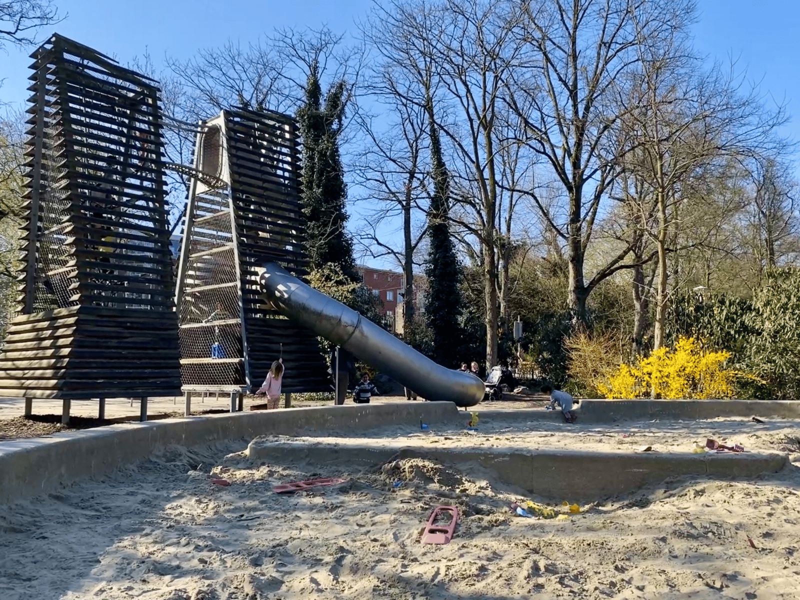 Large sand box with two wooden slat climbing towers and metal slides