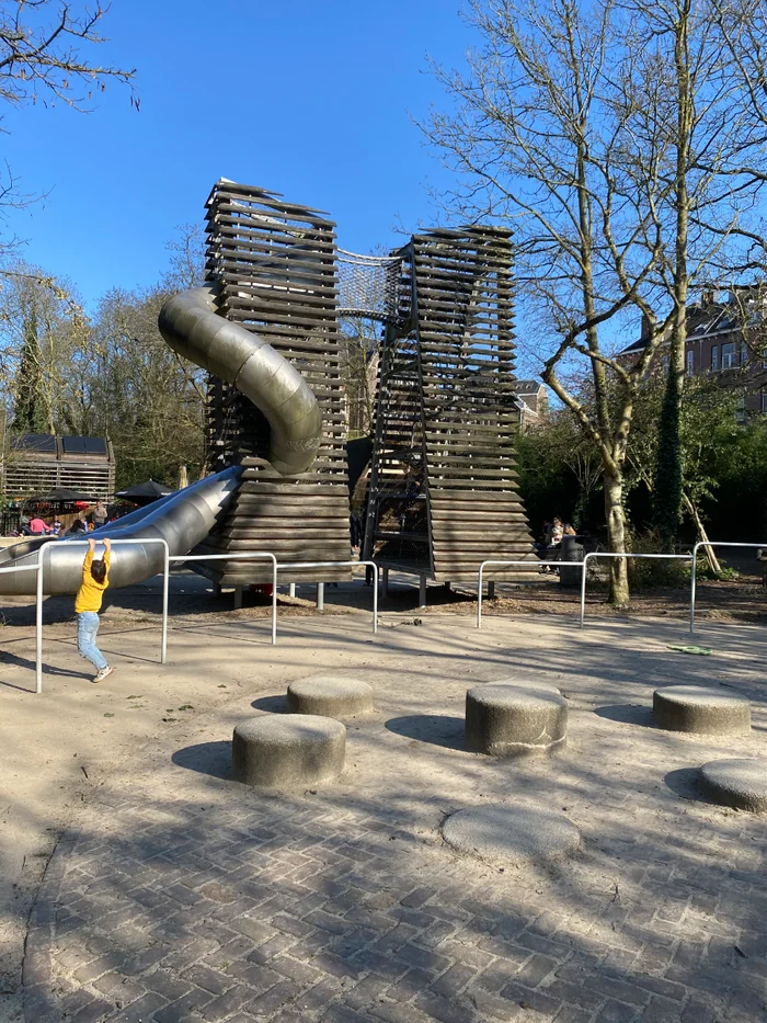 Two tall wooden towers with long spiral metal slide and stepping stones in the foreground