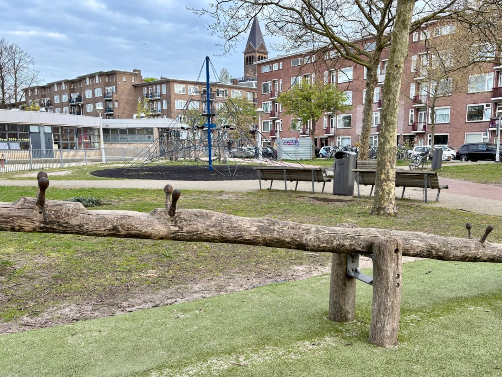 Large wooden balance beam with giant blue rope climbing tower in the distance