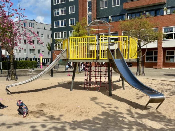 Yellow playground structure with climbing nets and metal slides on sand