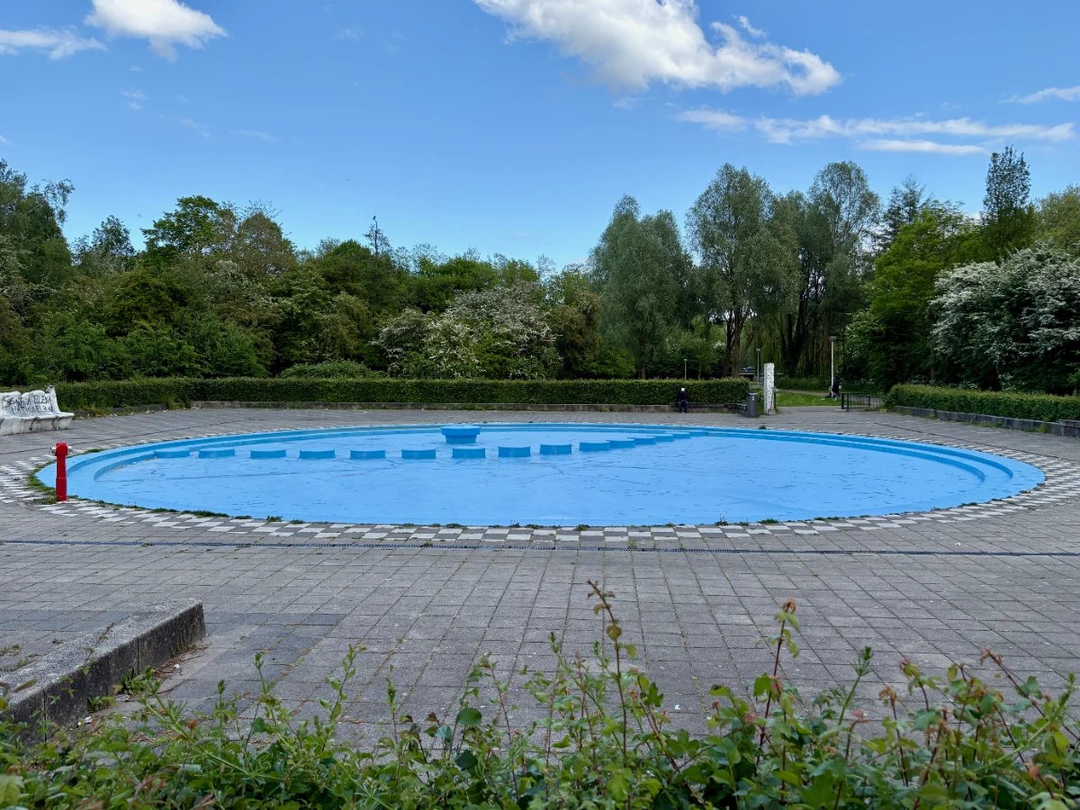Empty, bright blue painted paddling pool surrounded by concrete pavers and trees