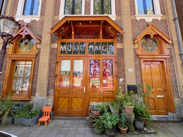 Theater entrance with ornate wooden doors and windows on brick facade with potted plants outside and signs in the window