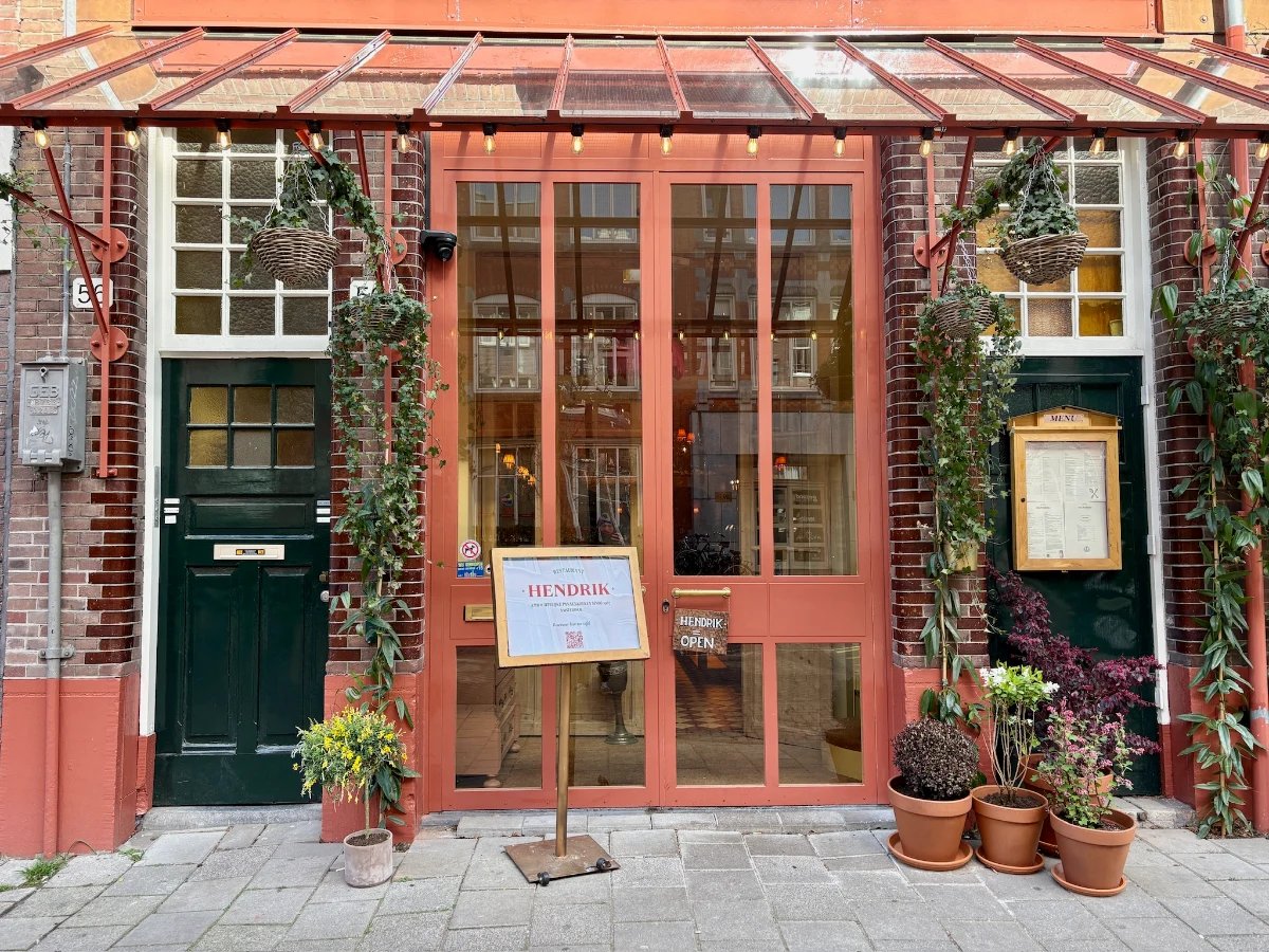 Terracotta-red storefront with black door, greenery, open sign and menu