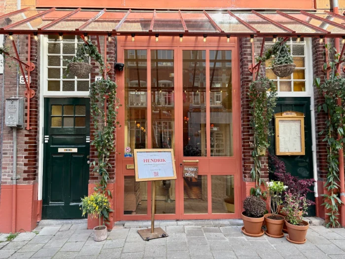 Terracotta-red storefront with black door, greenery, open sign and menu