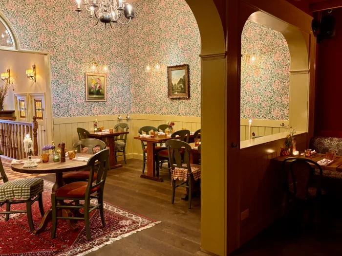 Cozy restaurant interior with floral wallpaper, cottage furniture, oil painting, and sconces