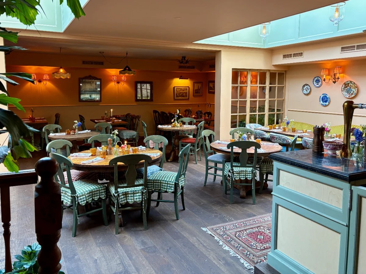 Restaurant dining room with green cottage furniture, floral and gingham decor, warm lighting and skylights overhead