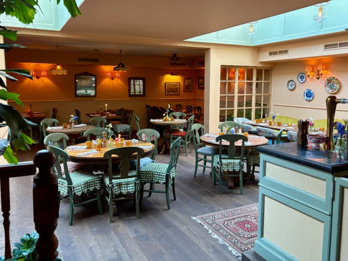 Restaurant dining room with green cottage furniture, floral and gingham decor, warm lighting and skylights overhead