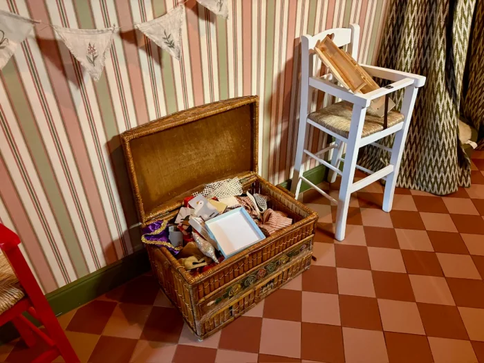 Toy box and high chair in a room with red checkered floors and red and green striped wallpaper