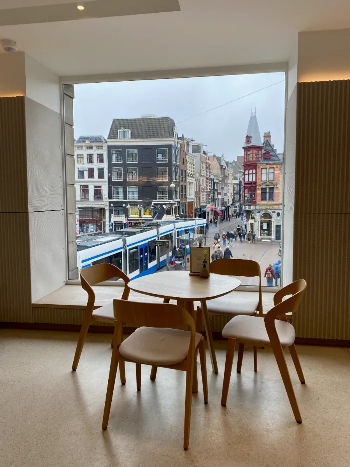 Scandinavian cafe table and chairs in front of large window with view of Amsterdam historic center with tram and people passing by below