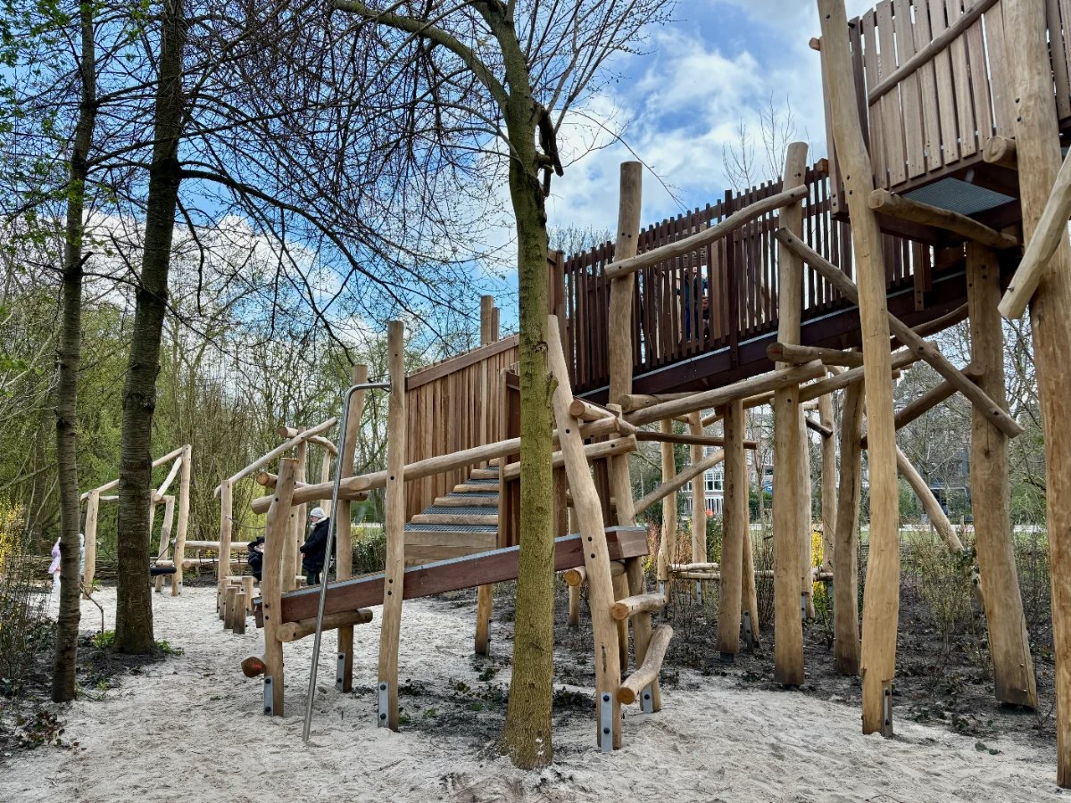 Large wooden climbing structure with ramps leading up to an elevated walkway supported by logs