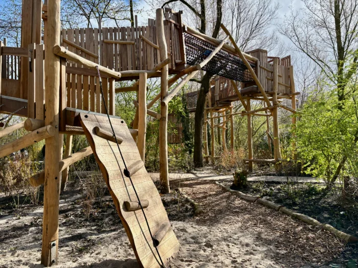 Climbing wall with rope leads to huge wooden walkway suspended through the trees