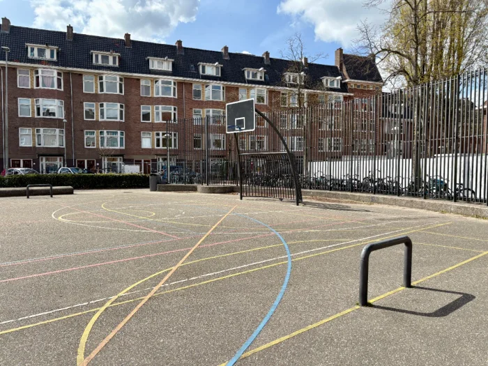 Outdoor sports court with basketball hoop and football goal with colorful lines on asphalt and buildings behind
