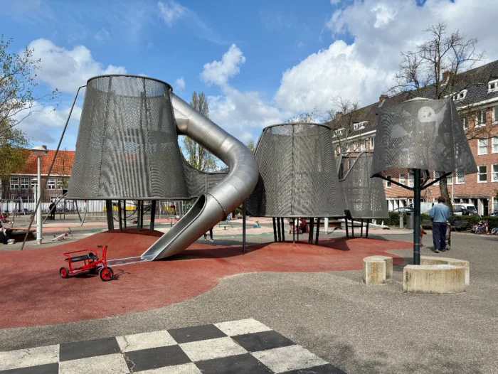 Modern metal play structure with mesh enclosure and long curving slide with red ground and blue skies