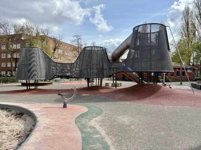 Backside of modern metal and mesh elevated play structure with metal rocker and sand box beside