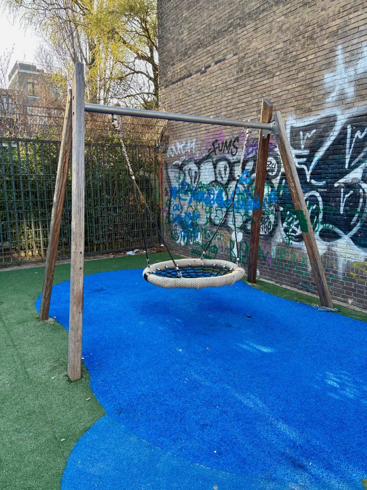 Nest swing on blue and green astroturf and grafitti-covered brick wall