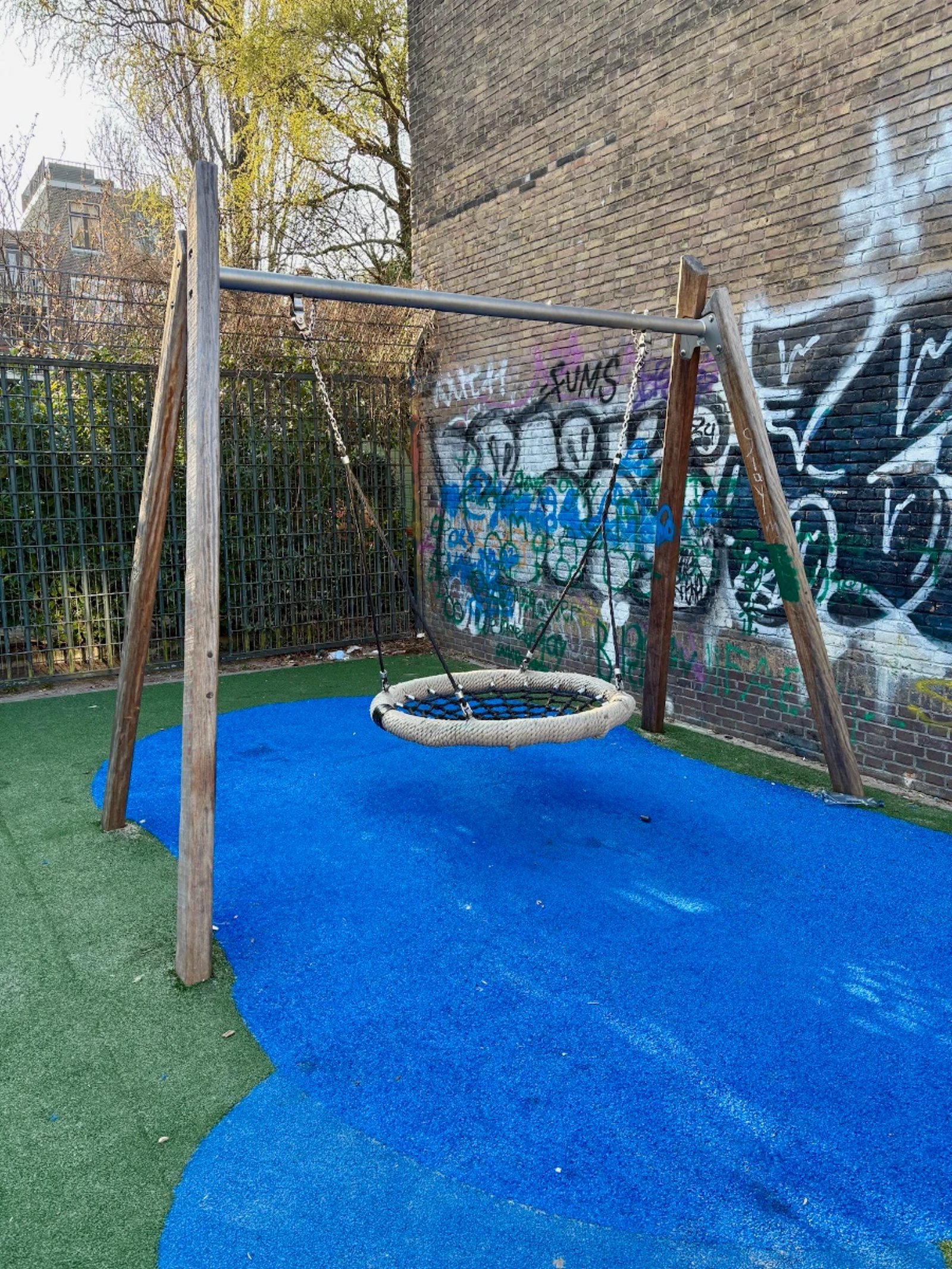 Nest swing on blue and green astroturf and grafitti-covered brick wall