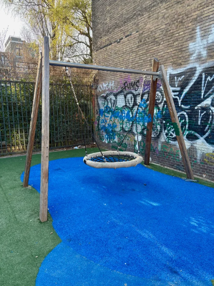 Nest swing on blue and green astroturf and grafitti-covered brick wall