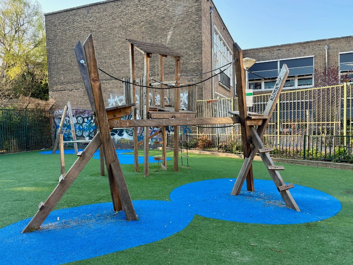 Playground with wooden and rope climbing structure on green and blue astro turf