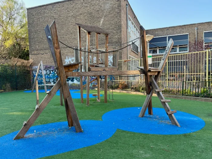 Playground with wooden and rope climbing structure on green and blue astro turf